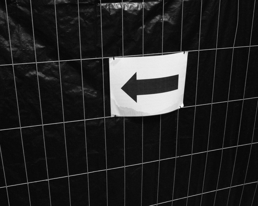 Black and white image of an arrow sign on a grid background indicating direction.