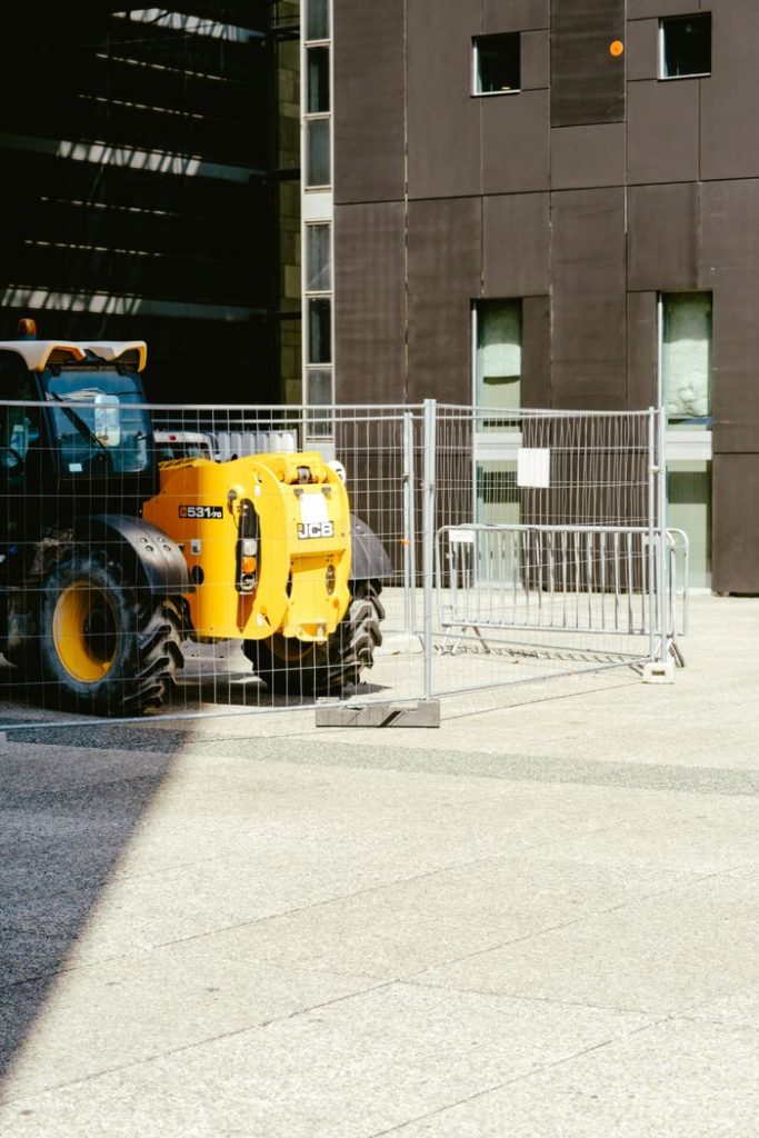A yellow tractor parked behind a metal fence at an urban construction site.