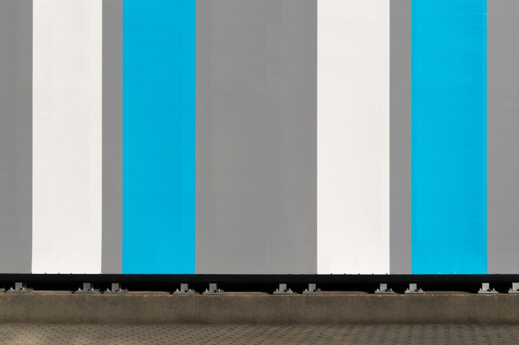 Abstract view of a modern building wall with vertical blue, gray, and white stripes.